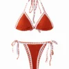 Front flat-lay of a textured orange bikini set with white trim featuring orange zigzag stitching, halter top, and side-tie bottoms.