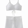 Macro close-up of white ribbed swimsuit fabric, inner lining, and a spaghetti strap connected via a metal ring.