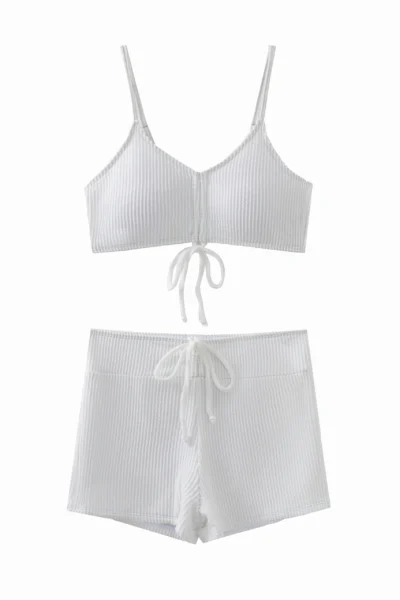 Macro close-up of white ribbed swimsuit fabric, inner lining, and a spaghetti strap connected via a metal ring.