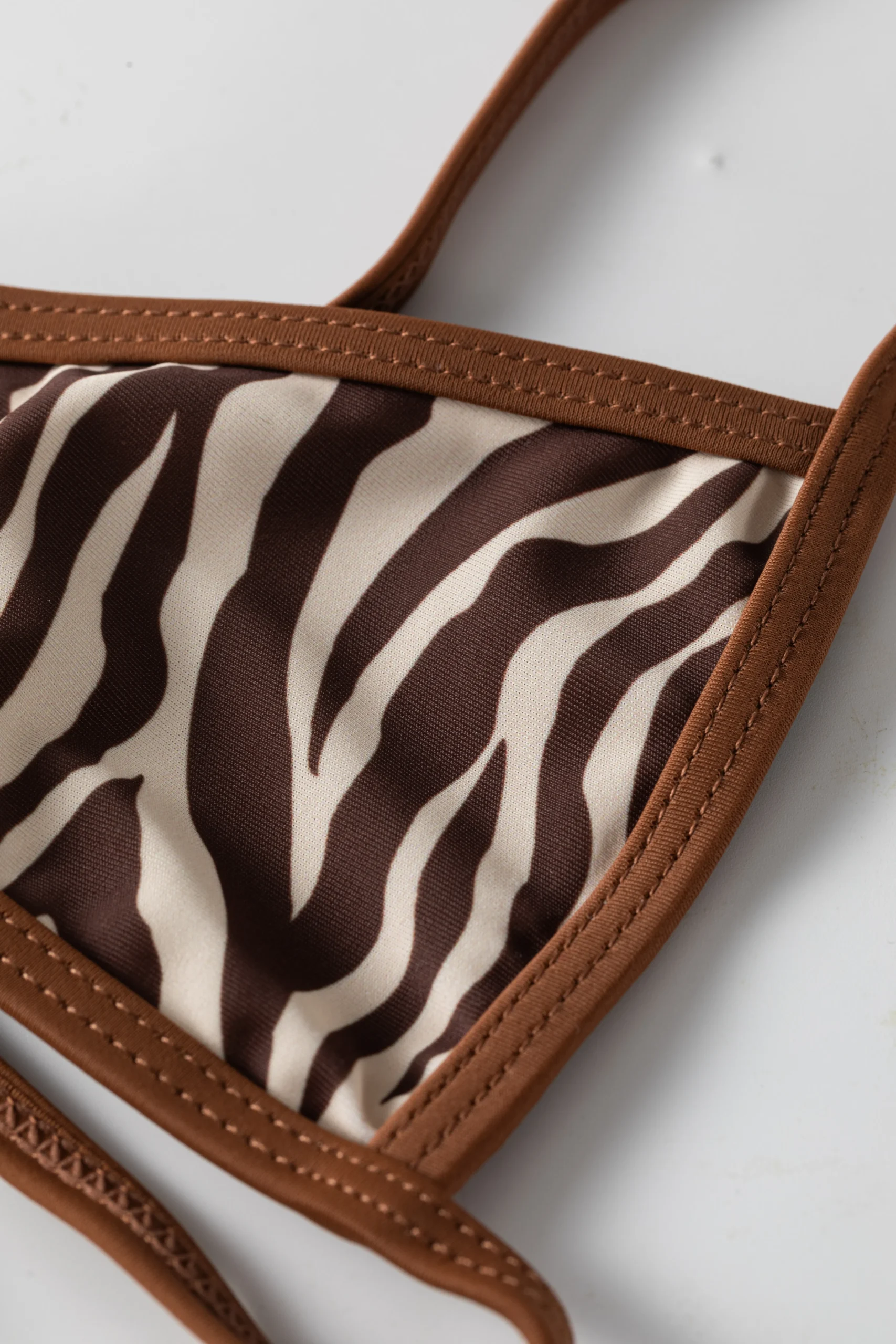 Macro close-up of the zebra print bikini top's neckline showing the brown contrast binding and stitched strap.