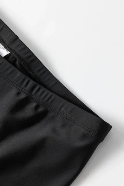 Front flat-lay of a black long-sleeve swimsuit top with floral raglan sleeves, a front zipper, and a peplum waist, paired with solid black full-length swim leggings.