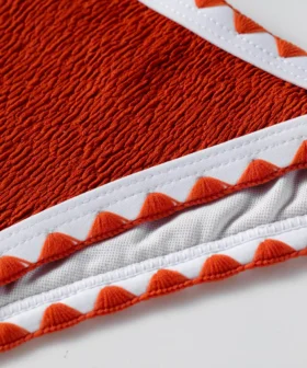Macro close-up of textured orange bikini fabric, white edge binding, orange zigzag stitching, and white inner lining.