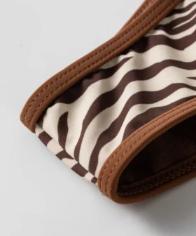 Macro close-up of the zebra print bikini edge showing the brown binding and an opening revealing the brown inner lining.