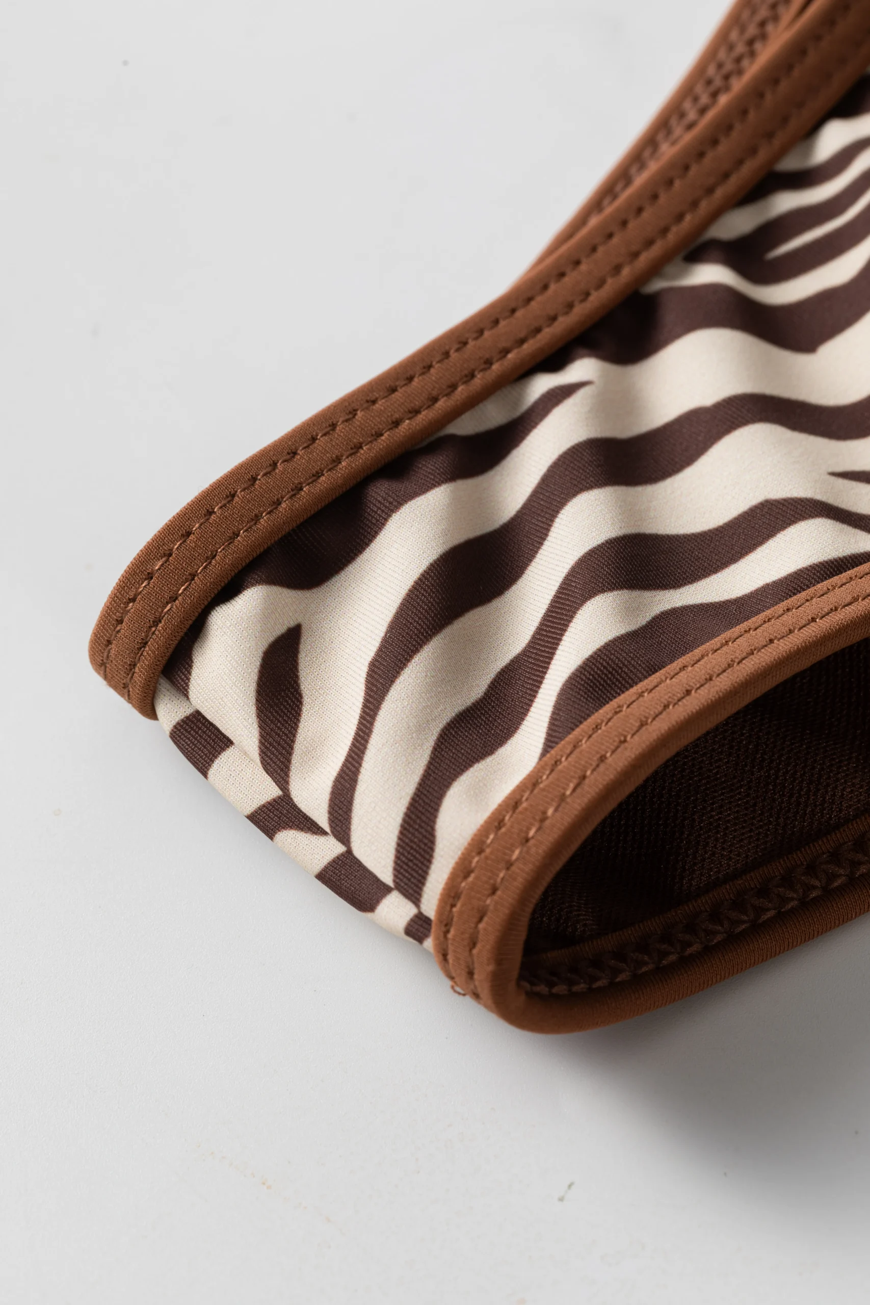 Macro close-up of the zebra print bikini edge showing the brown binding and an opening revealing the brown inner lining.