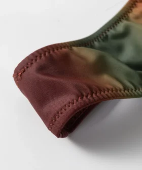 Macro close-up of a fabric edge on the ombre bikini showing zigzag stitching and the transition between rust and olive colors.