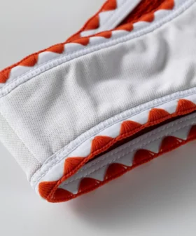 Macro close-up of the white inner lining, white edge binding, and decorative orange zigzag stitching on the bikini.