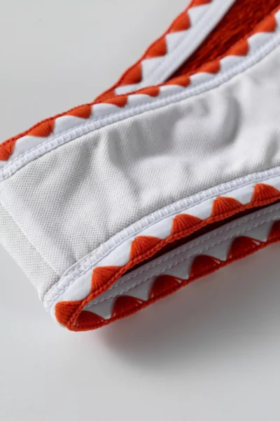Macro close-up of the white inner lining, white edge binding, and decorative orange zigzag stitching on the bikini.