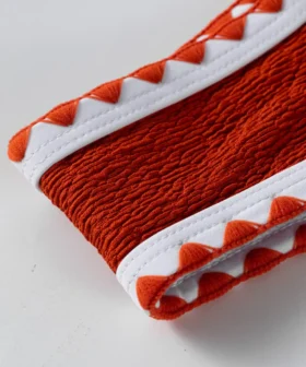 Macro close-up of the corner of the textured orange bikini cup featuring white binding and orange zigzag trim.