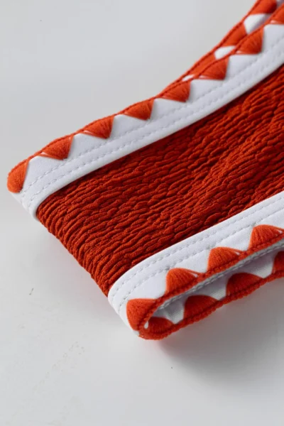 Macro close-up of the corner of the textured orange bikini cup featuring white binding and orange zigzag trim.