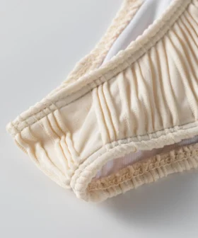 Macro close-up of a white flat elastic strap attached to white ribbed fabric, showing zigzag stitching.