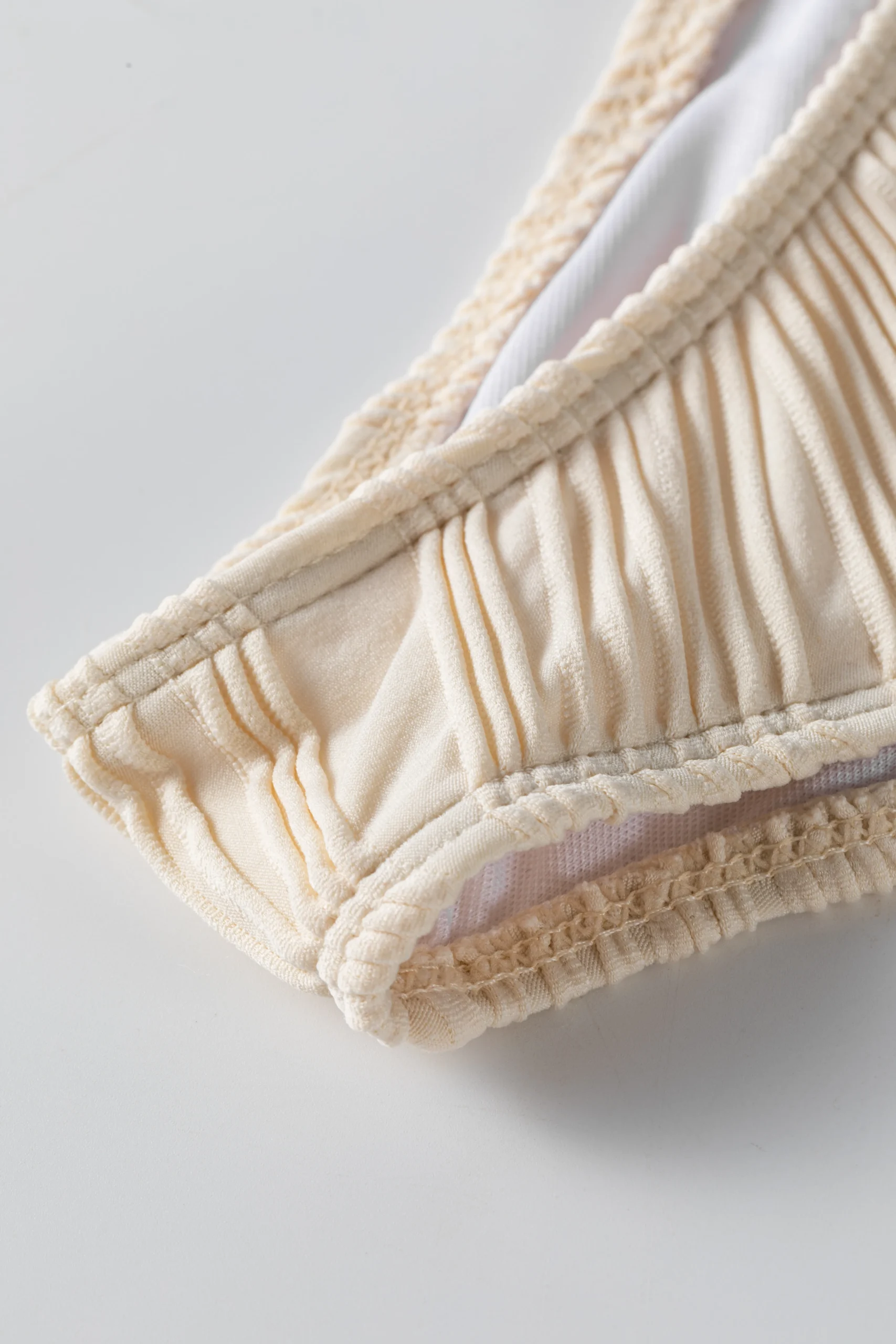 Macro close-up of a white flat elastic strap attached to white ribbed fabric, showing zigzag stitching.