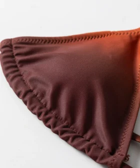 Macro close-up of a bikini top cup edge featuring gathered fabric, zigzag stitching, and a rust-to-orange color fade.