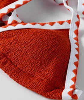 Macro close-up of a white tie string attached to the corner of a textured orange bikini cup.