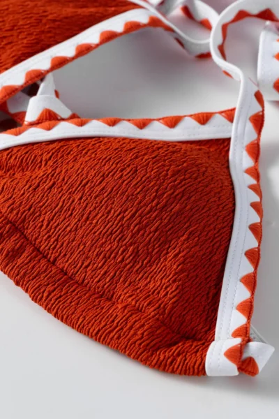 Macro close-up of a white tie string attached to the corner of a textured orange bikini cup.