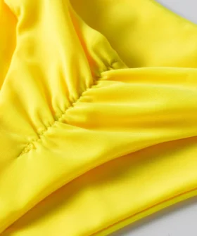 Macro close-up of ruched stitching detail on solid yellow bikini fabric.