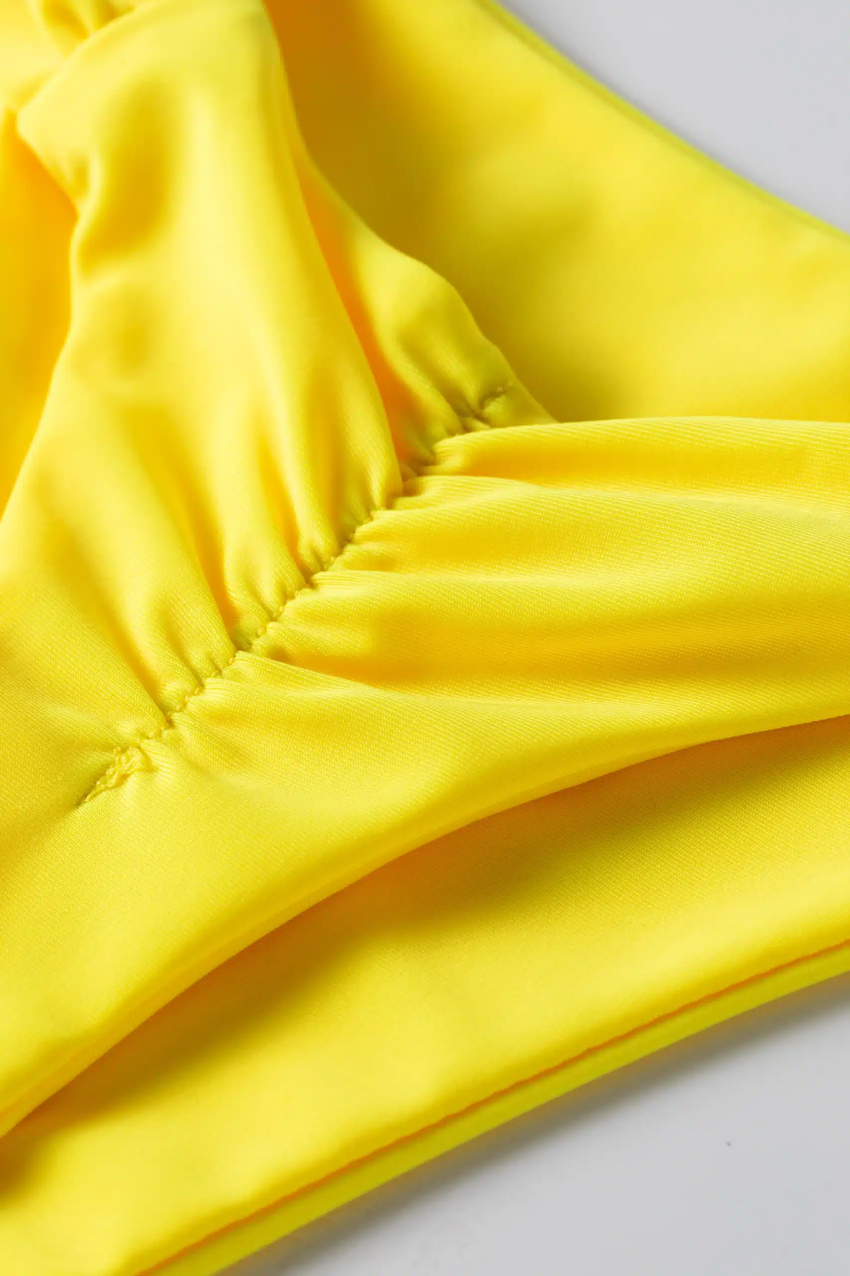 Macro close-up of ruched stitching detail on solid yellow bikini fabric.
