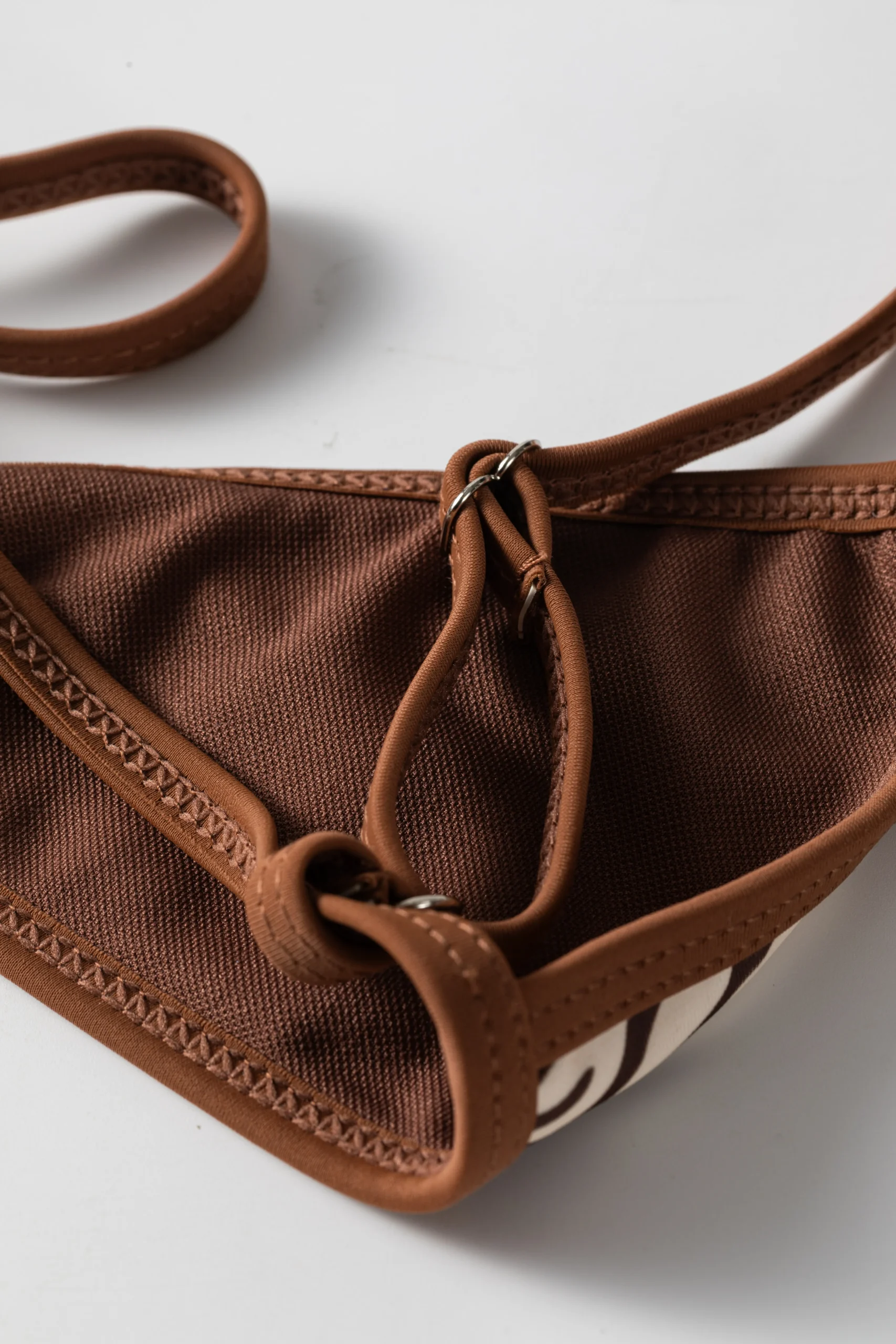 Macro close-up of the back fabric of the bikini top showing the brown mesh lining, binding, and metal ring for the strap.