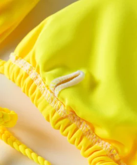 Macro close-up of the tie-string eyelet opening on a yellow bikini top, with the twisted strap.
