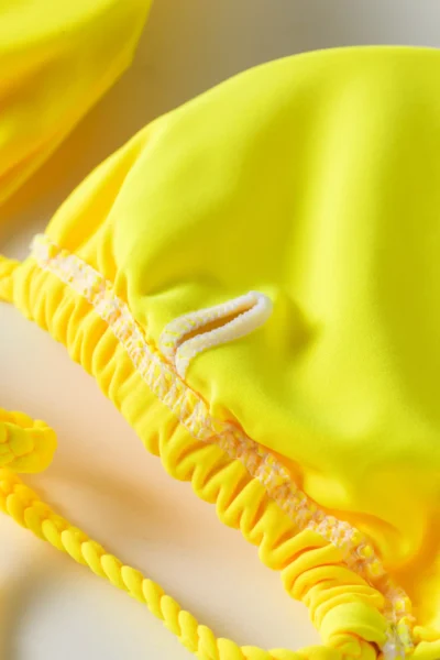 Macro close-up of the tie-string eyelet opening on a yellow bikini top, with the twisted strap.