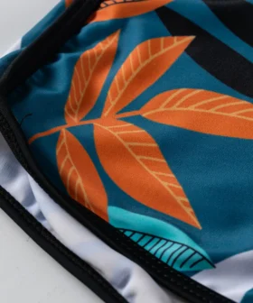 Front flat-lay of a black halter bikini top with a deep V-neck and tie back, paired with teal and orange botanical print swim shorts and a front drawstring.