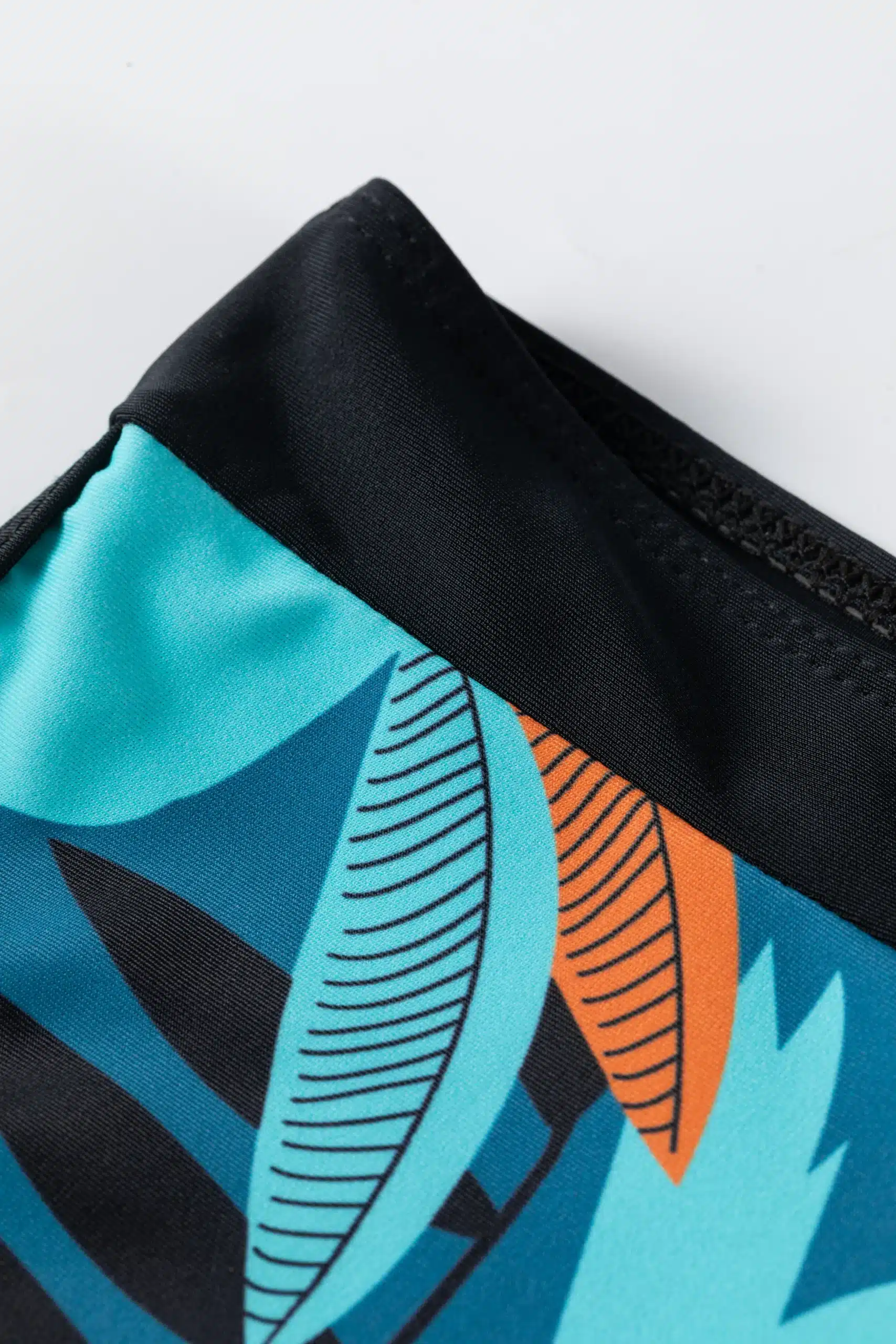 Macro close-up of the black drawstring ties tied into a knot on the front of the bikini top, resting against the orange and teal printed hem.