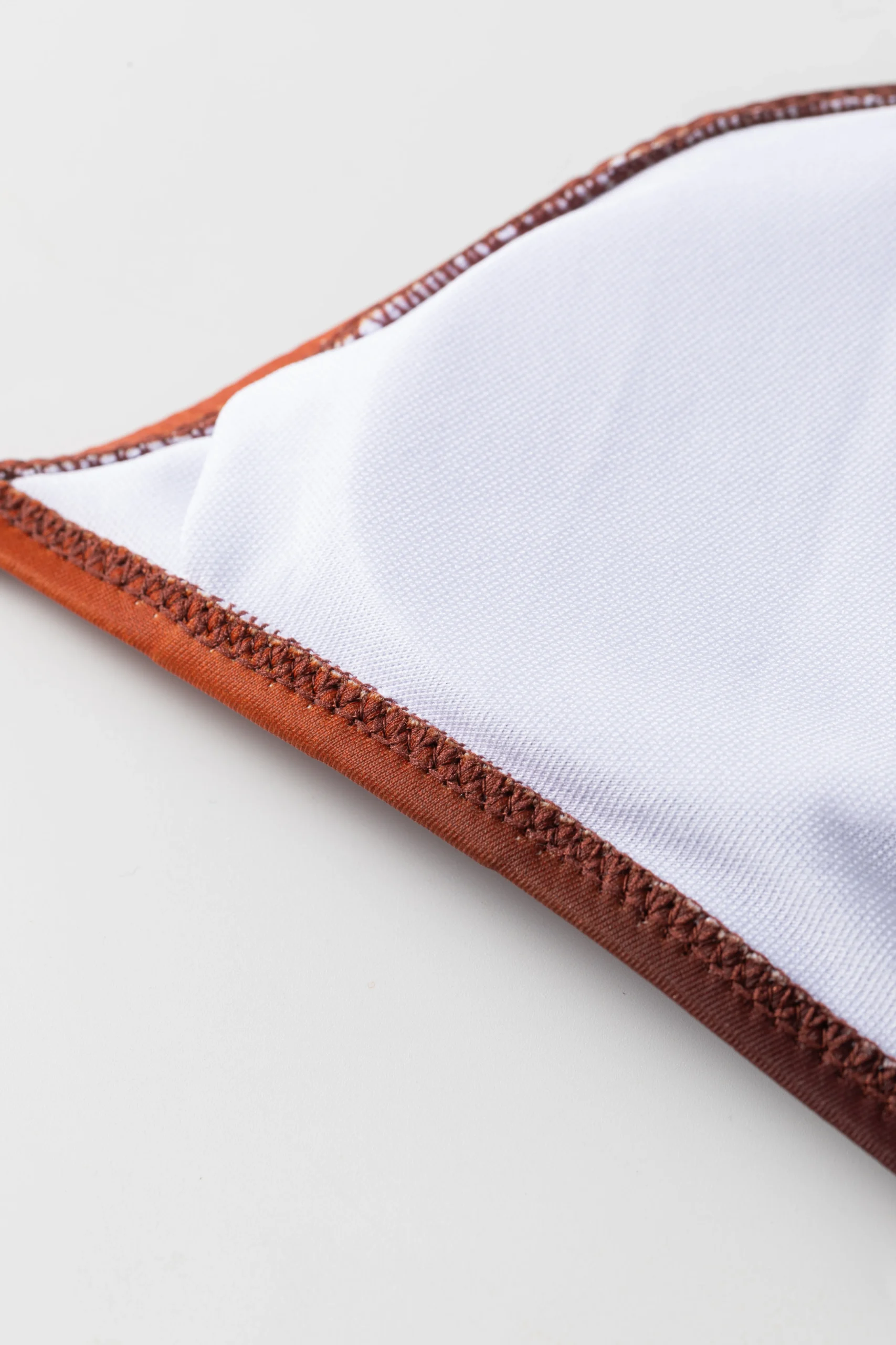 Macro close-up of the bikini garment's white inner lining, revealing the neat zigzag stitching along the edge.