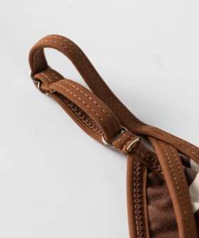 Macro close-up of a brown flat elastic strap threaded through a metal slider, featuring zigzag edge stitching.
