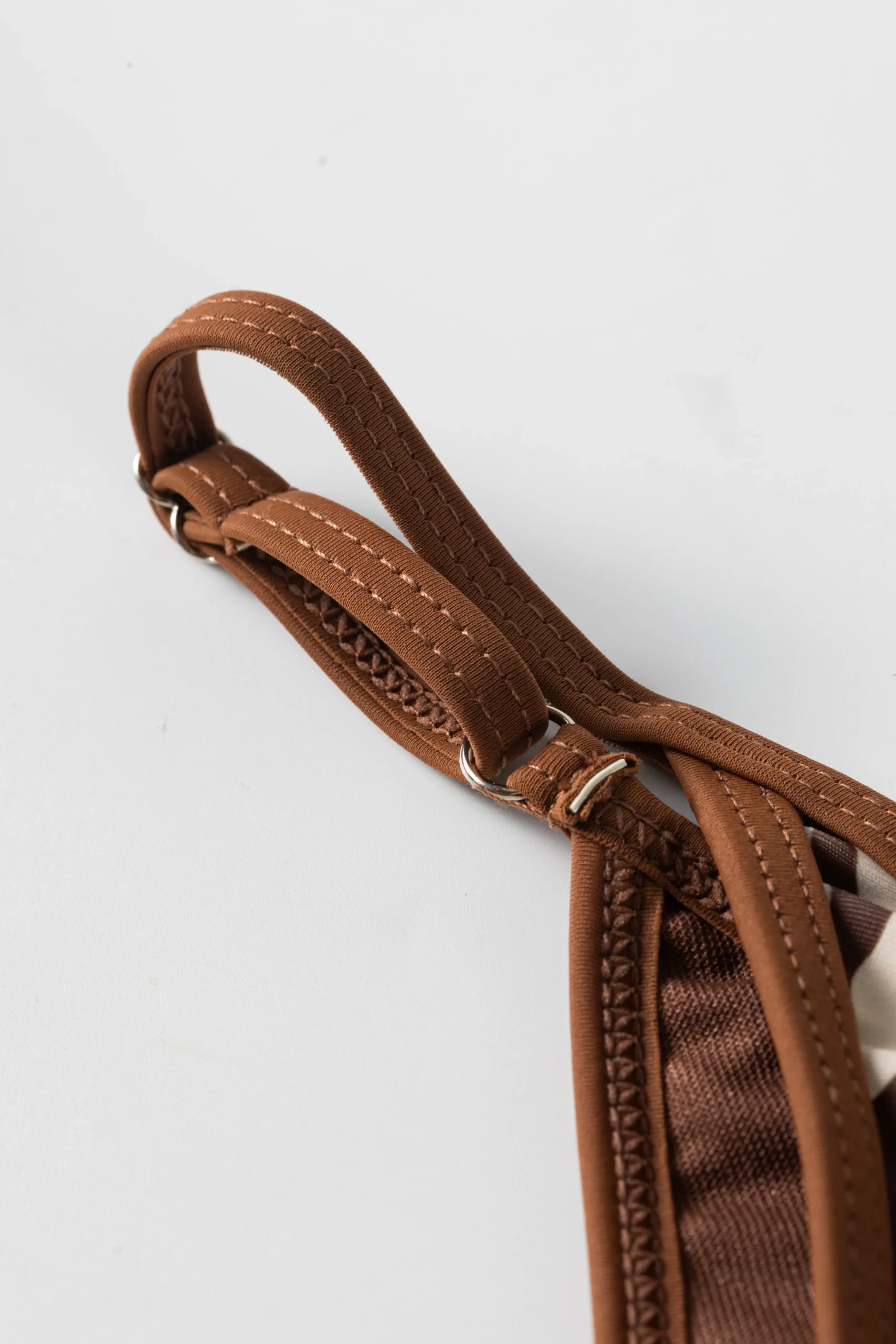 Macro close-up of a brown flat elastic strap threaded through a metal slider, featuring zigzag edge stitching.
