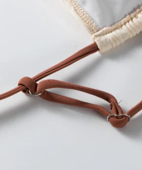 Front flat-lay of an ivory textured bikini set with brown spaghetti straps, a gold front ring, and multi-strap side bottoms.