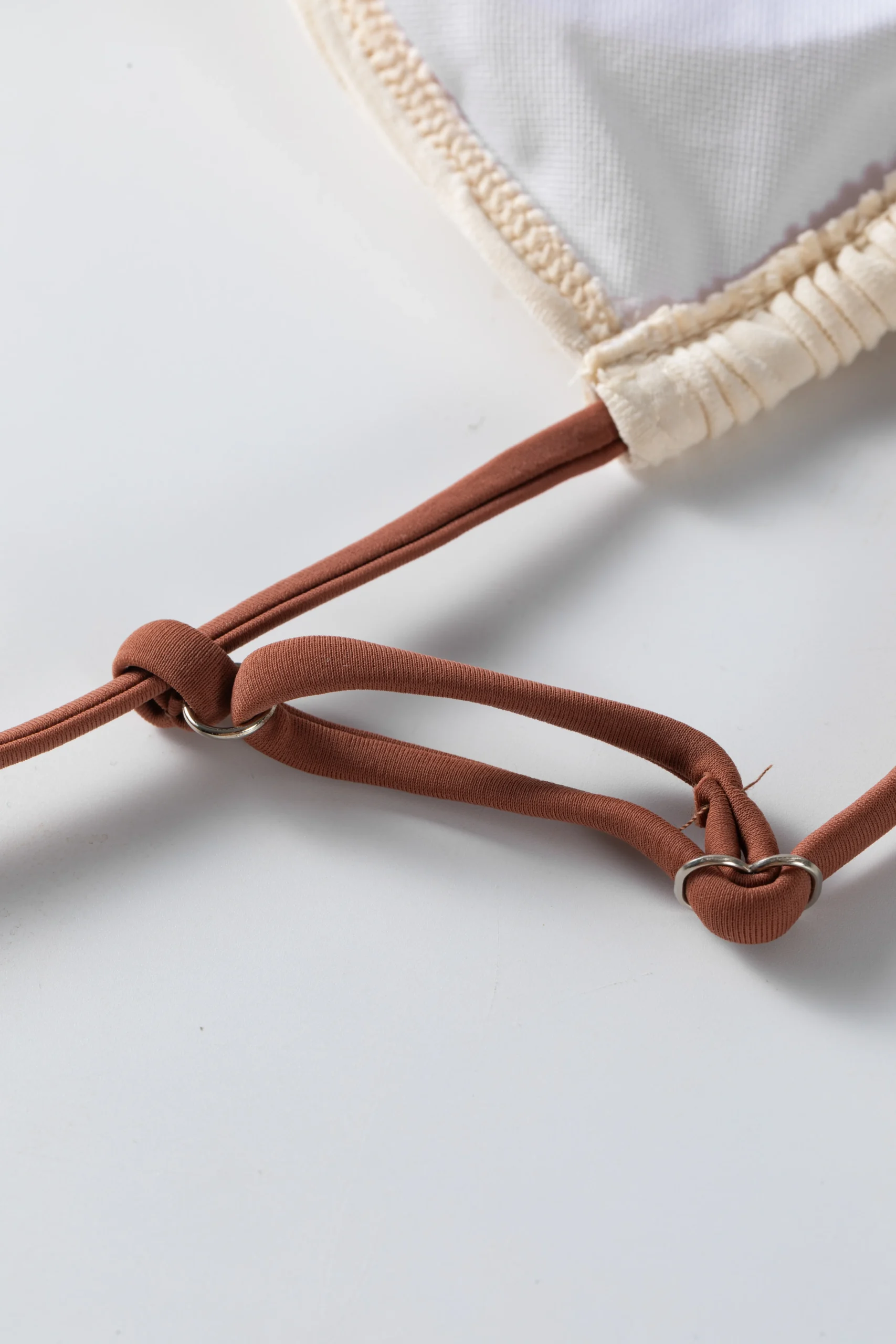 Front flat-lay of an ivory textured bikini set with brown spaghetti straps, a gold front ring, and multi-strap side bottoms.