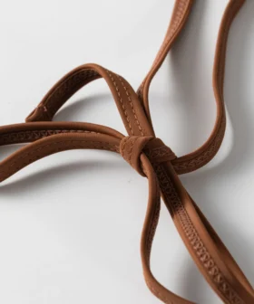 Macro close-up of the brown flat elastic bikini straps tied into a knot, highlighting the edge stitching.
