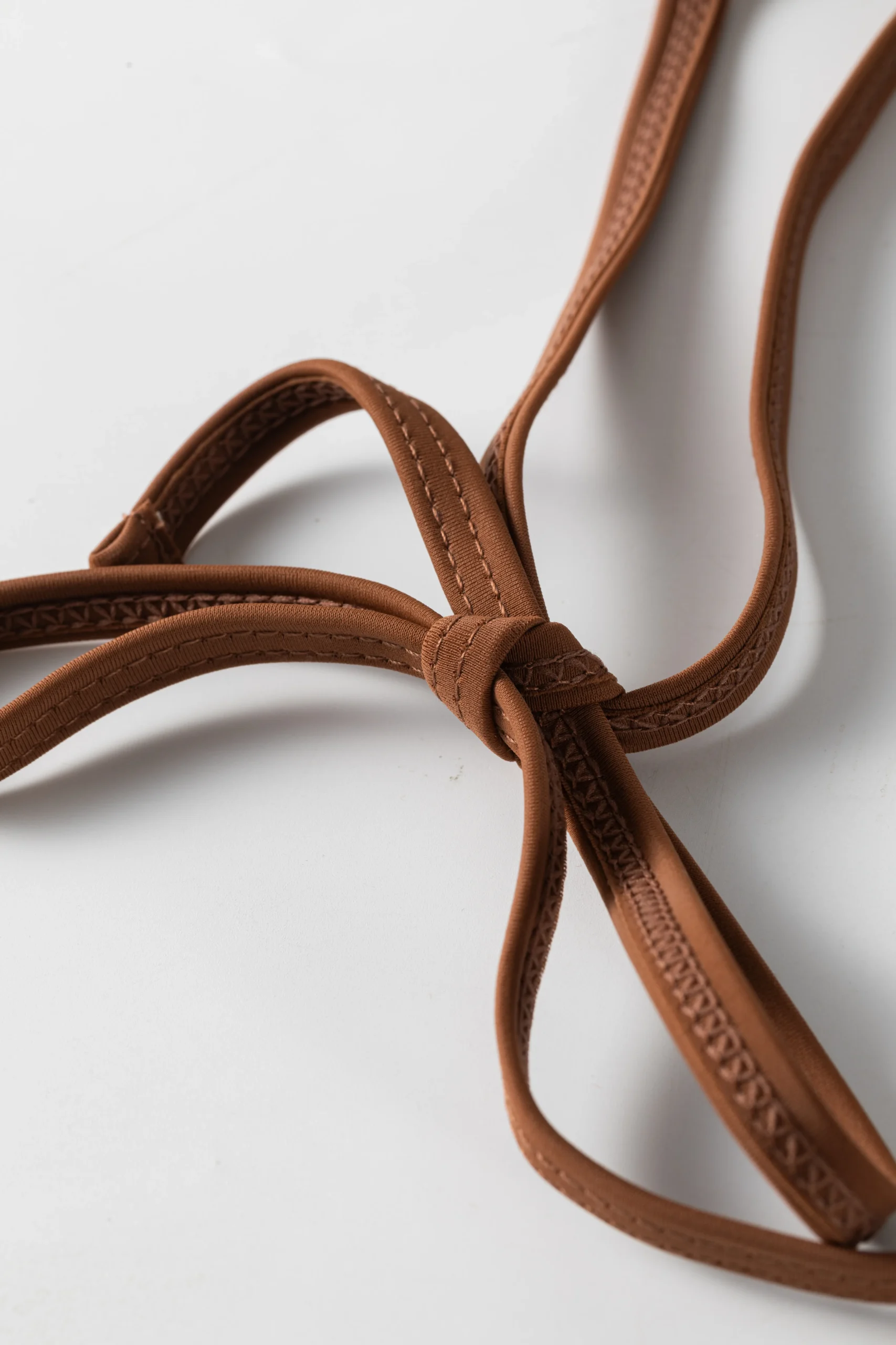 Macro close-up of the brown flat elastic bikini straps tied into a knot, highlighting the edge stitching.