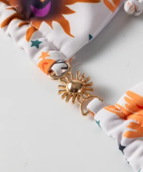 Macro close-up of a gold sun-shaped metal connector clasp joining two pieces of patterned bikini fabric.