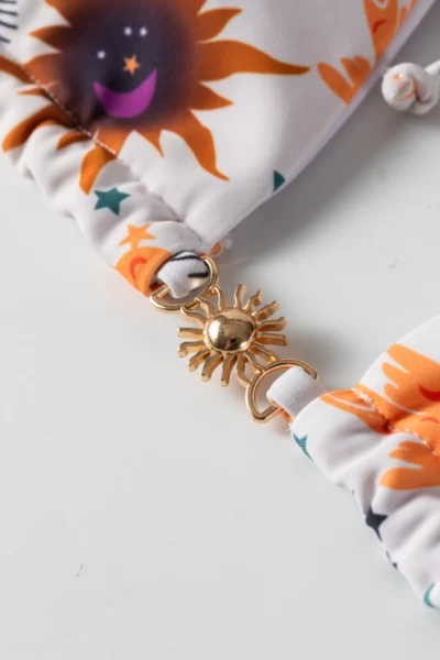 Macro close-up of a gold sun-shaped metal connector clasp joining two pieces of patterned bikini fabric.