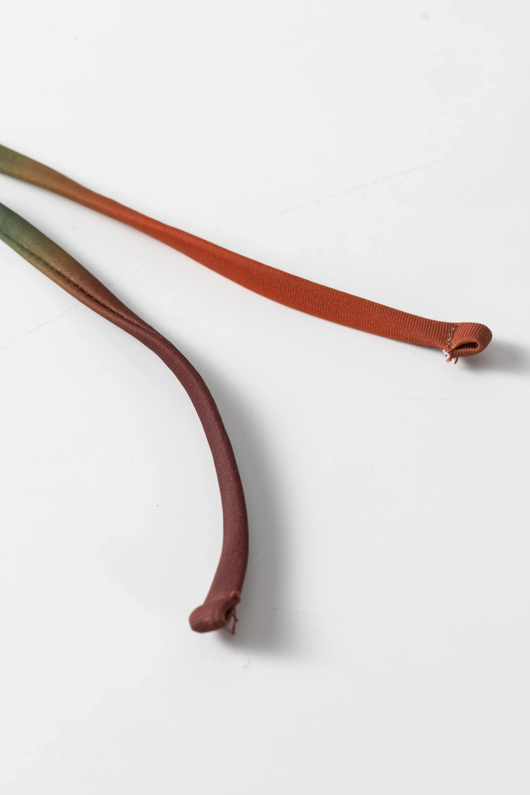 Macro close-up of the ends of two thin tubular ombre bikini tie strings, showing the folded and stitched tips.