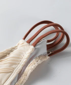 Macro close-up of the ruched ivory bikini fabric, white inner lining, and textured edge stitching.