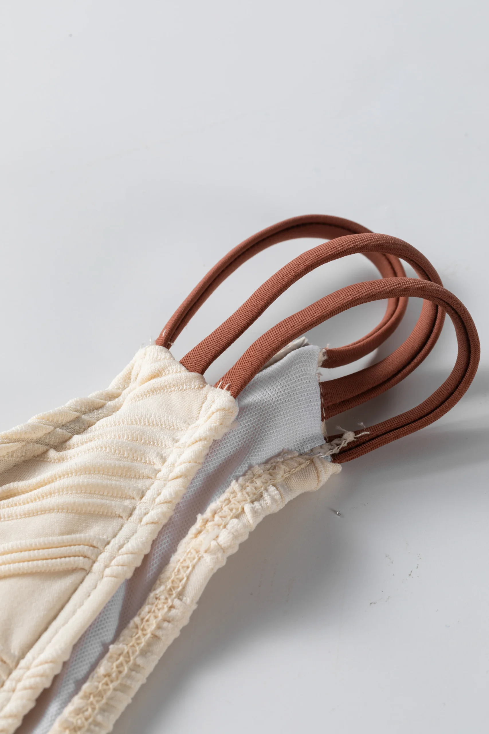 Macro close-up of the ruched ivory bikini fabric, white inner lining, and textured edge stitching.