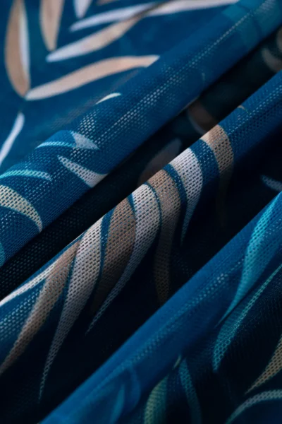 Macro close-up of folded semi-sheer mesh fabric with a blue and pink abstract pattern, highlighting its fine woven texture.