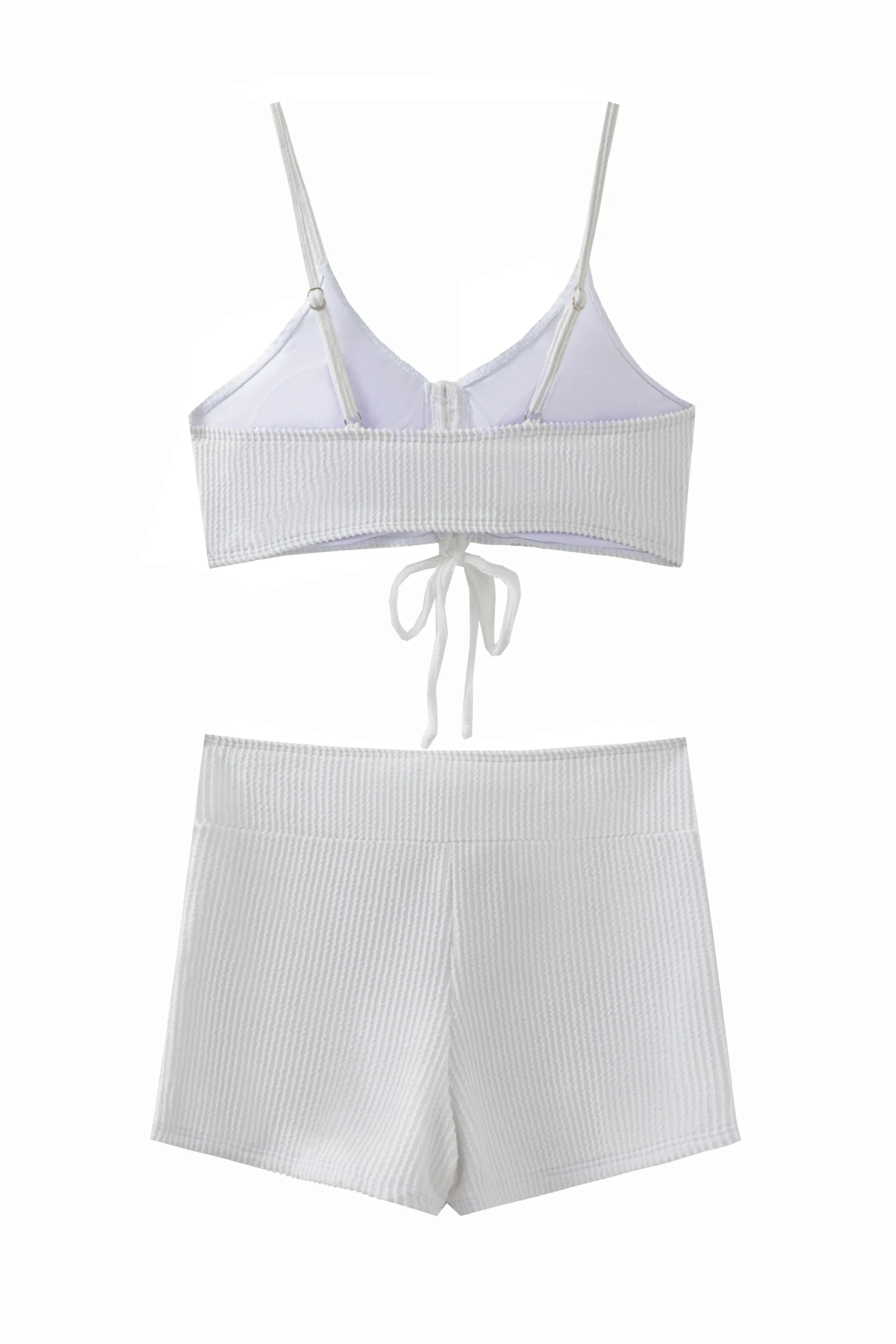 A front flat-lay product shot of a solid white two-piece swimsuit. The top features a slight halter neck with thin tie strings and is bordered with ruffle details along both the top and bottom edges. The matching high-cut bottoms feature side-tie strings and a ruffle trim along the waistband.