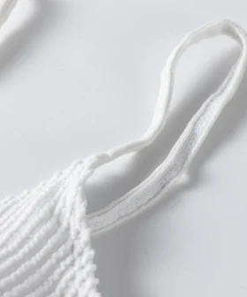 Macro close-up of thin white straps tied through a metal ring on white ribbed swimwear.