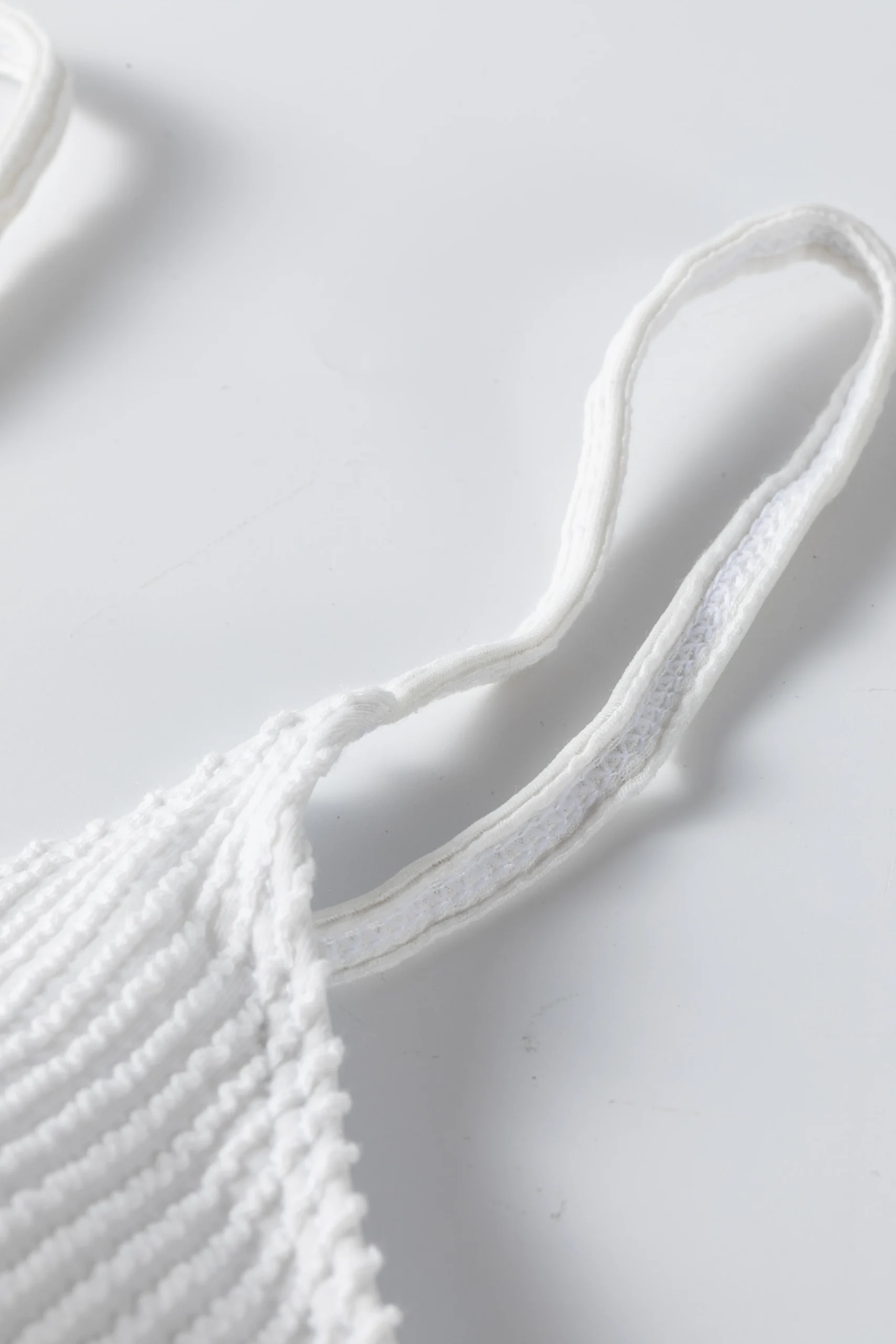 Macro close-up of thin white straps tied through a metal ring on white ribbed swimwear.