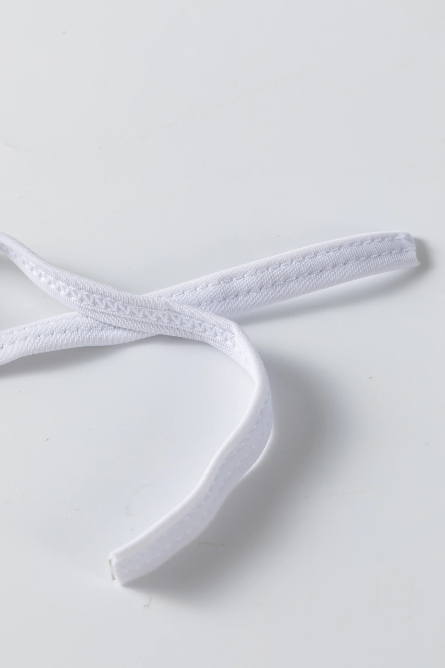 Close-up detail of tightly gathered white ruffle trim on solid white bikini fabric.