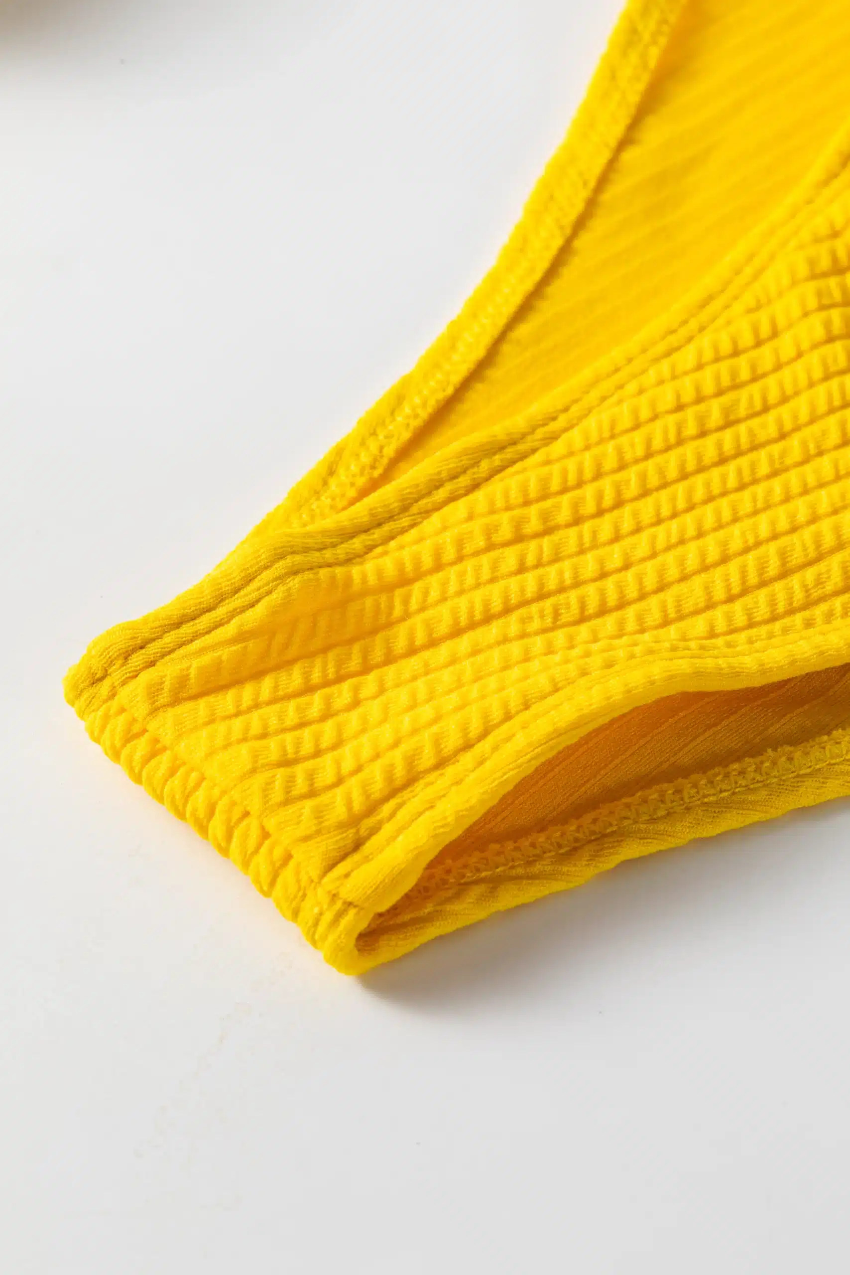 Close-up of yellow ribbed bikini bottom edge showing white inner lining and hem stitching.