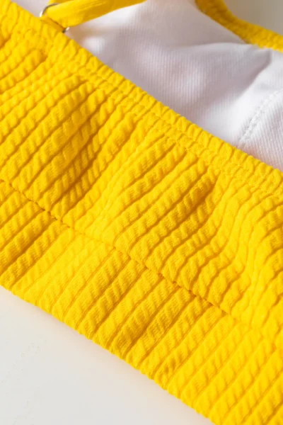 Macro detail of yellow ribbed bikini top showing white inner lining, hem, and silver metal ring. SEO: