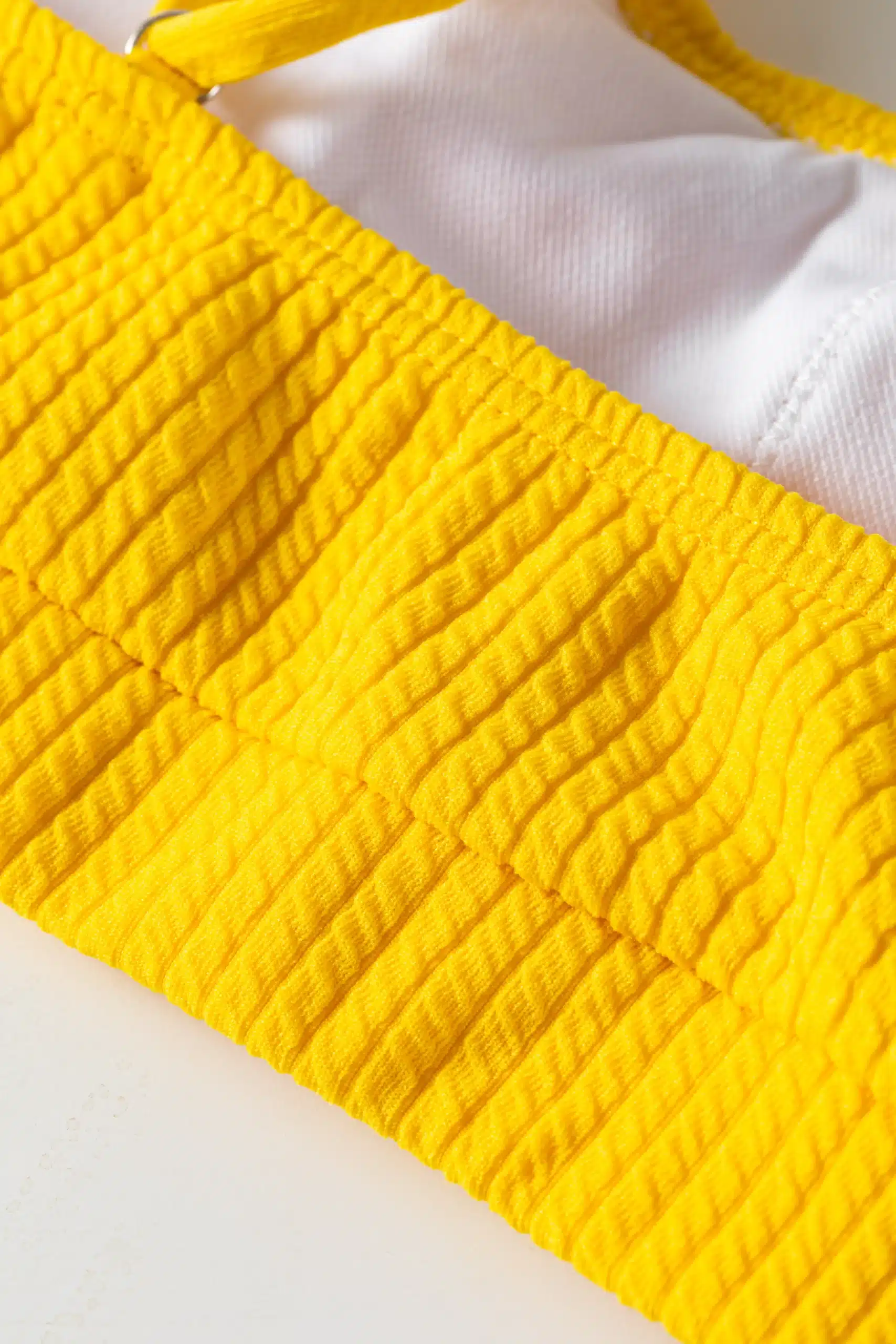 Macro detail of yellow ribbed bikini top showing white inner lining, hem, and silver metal ring. SEO:
