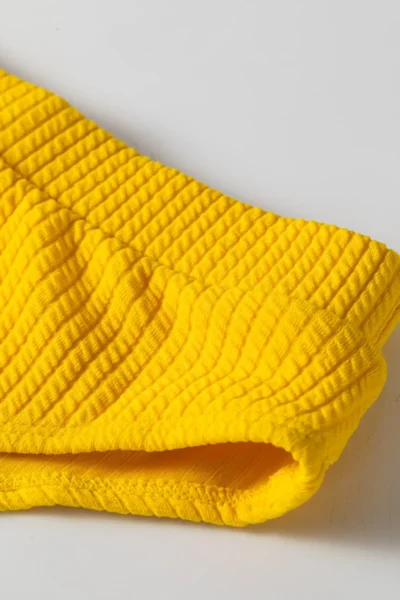 Close-up of yellow ribbed bikini fabric texture and gusset area with white lining.