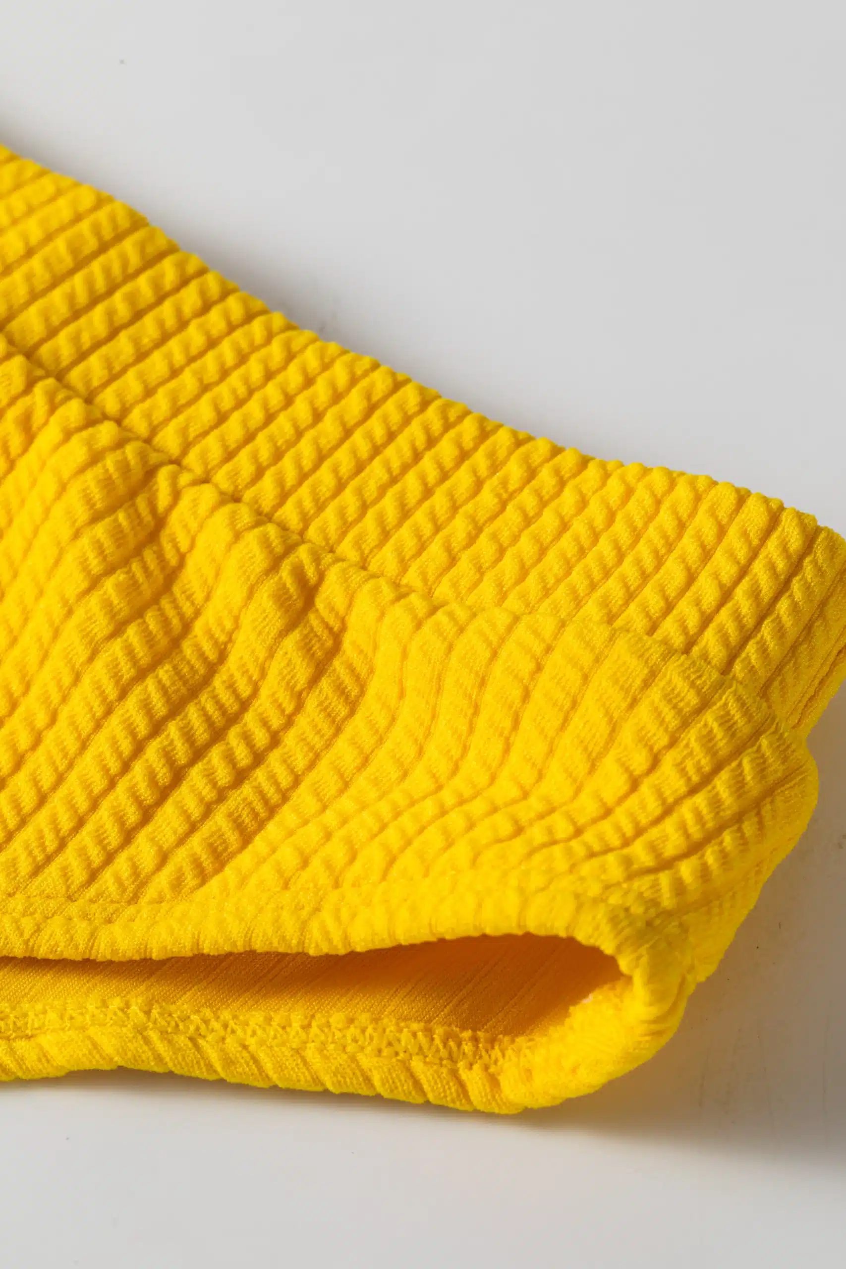 Close-up of yellow ribbed bikini fabric texture and gusset area with white lining.