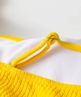 Detail of thin yellow bikini strap looping through a silver metal ring attached to the white-lined top.