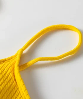 Close-up of the thin elastic yellow shoulder strap sewn into the ribbed fabric of the bikini top.