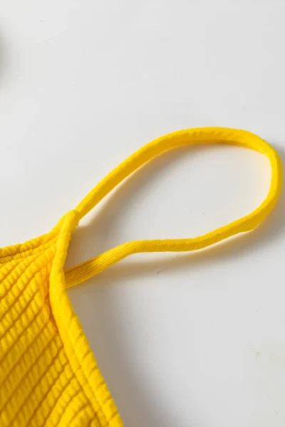 Close-up of the thin elastic yellow shoulder strap sewn into the ribbed fabric of the bikini top.